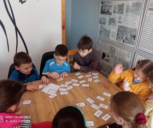 Zdjęcie przedstawia grupę dzieci wykonujących zadnie, podczas lekcji bibliotecznej.