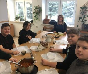 Grupa dzieci siedzi przy nakrytym do posiłku stole, w centrum pani dyrektor