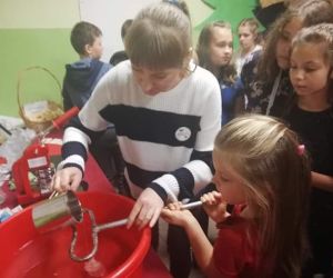 Na pierwszym planie animator leje wosk przez dużą dziurkę od dużego klucza, który trzyma mała dziewczynka. W tle bawi się kilkoro dzieci.