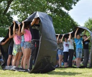 Na zdjęciu znajdują się dzieci, które są podzielone na dwie grupy i uczestniczą w wyścigach tunelowych.