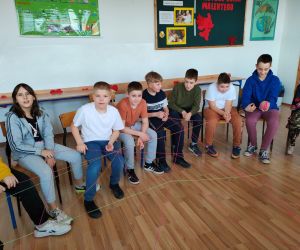 Grupa osób siedzi w kole wewnątrz budynku.