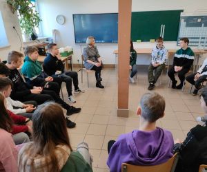 Grupa osób siedzi w kole wewnątrz budynku.