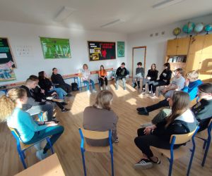 Grupa osób siedzi w kole wewnątrz budynku.