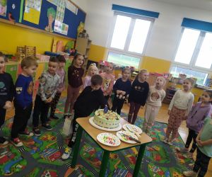 Marcel stoi przy torcie a dzieci śpiewają.