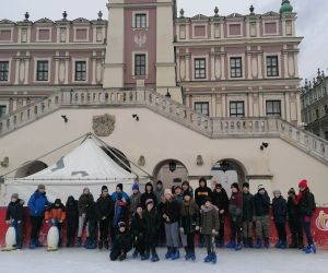 Grupa uczniów z nauczycielami na lodowisku na tle ratusza w Zamościu