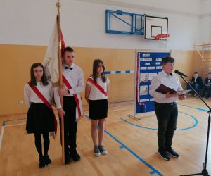 Uczeń stoi przy mikrofonie, obok stoi Poczet sztandarowy