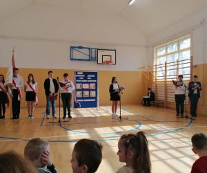 Pięcioro uczniów stoi przy mikrofonach, obok stoi Poczet sztandarowy