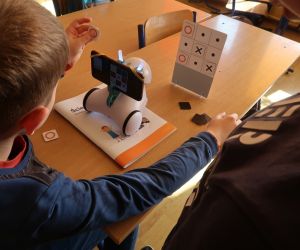 Uczeń gra ze sztuczną inteligencją i umieszcza magnetyczne elementy gry na planszy.