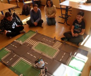 Grupa uczniów obserwuje przemieszczanie się robota po macie Smart City.