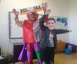 Chłopiec z maską śpiewa i tańczy, a klauna z tyłu trzyma napis Polska