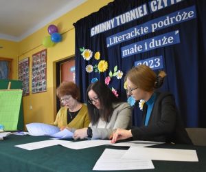 Zdjęcie przedstawia trzy dorosłe osoby siedzące przy stole, czytające cos na kartce.