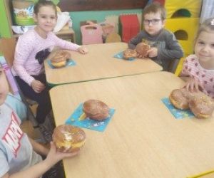 dzieci siedzą przy stole, jedzą pączki