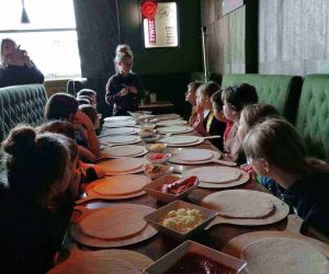 Uczniowie z instruktorką przy stole przed rozpoczęciem warsztatów z pieczenia pizzy