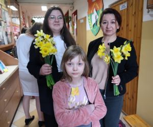 Opiekun Samorządu Uczniowskiego i uczennice z pękami żółtych żonkili w szkole