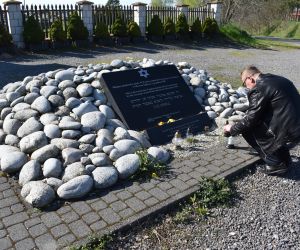 Osoba zapala znicz pod pomnikiem.