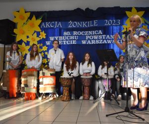 Zespół śpiewa i gra na scenie. Osoba przemawia do mikrofonu.