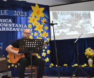 Występ solowy, mężczyzna siedzi na scenie i gra na gitarze.