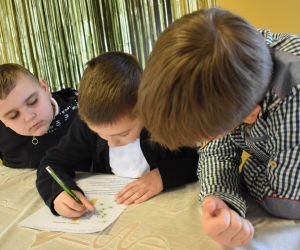 Na zdjęciu widocznych jest trzech chłopców piszących na kartce.
