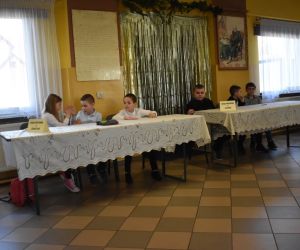 Zdjęcie przedstawia uczniów siedzących przy stołach w trakcie konkursu.