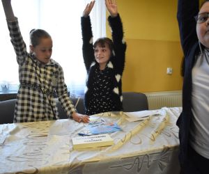 Na zdjęciu widoczna jest trójka dzieci z podniesionymi rękami, zgłaszająca się.