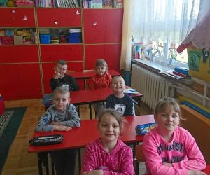 Zdjęcie przedstawia dzieci siedzące w ławkach.