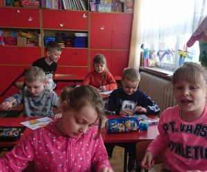 Zdjęcie przedstawia dzieci siedzące w ławkach.