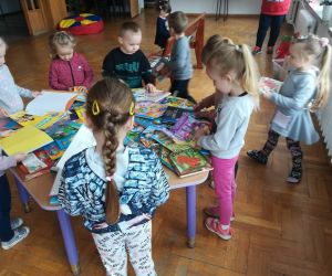 Zdjęcie przedstawia dzieci przeglądające książki rozłożone na stoliku. 