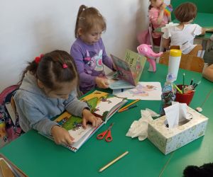 Na zdjęciu widoczne są dzieci siedzące przy stoliku czytające książkę.