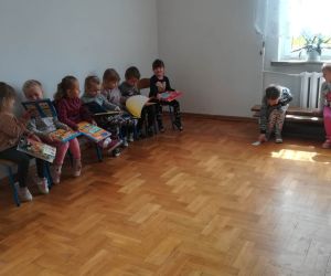 Na zdjęciu widoczne są dzieci siedzące wewnątrz budynku czytające książki.
