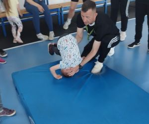 Trener pomaga przedszkolakowi wykonać przewrót w przód