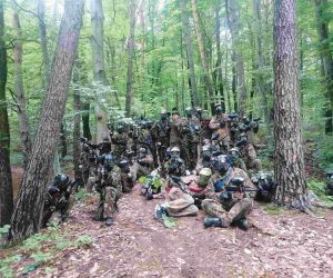 Grupa uczniów w mundurach, kaskach i maskach w lesie