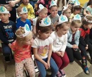 Przedszkolaki siedzą na apelu poświęconym ekologii. Mają założone na głowy opaski z planetą Ziemią.