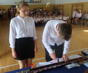Uczeń klasy ósmej  wbija pamiątkowy gwóźdź w drzewce sztandaru.