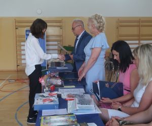 Dyrektor szkoły i wychowawczyni klasy ósmej  wręczają świadectwo uczennicy klasy ósmej.