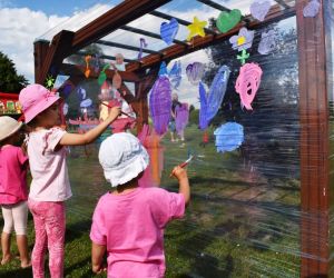 Grupa dzieci na świeżym powietrzu maluje obraz na foli.