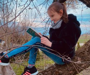 Dziewczynka czytająca książkę, siedząca na drzewie