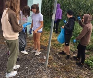 Kilkoro uczniów zbiera śmieci koło przystanku autobusowego