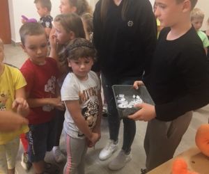 Uczeń trzyma w ręku losy na loterię fantową, a przed nim stoją dzieci