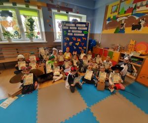 Dzieci przebrane za postaci z bajek. Siedzą na podłodze i trzymają w rękach dyplomy pamiątkowe z konkursu.