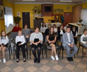 Zdjęcie przedstawia młodzież i dorosłych słuchających recytacji.