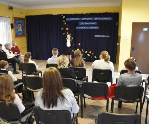 Zdjęcie przedstawia młodzież i dorosłych słuchających recytacji.