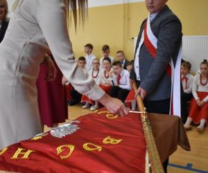 Dyrektor szkoły przybija gwóźdź pamiątkowy do drzewca sztandaru szkoły