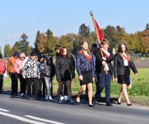 Kolumna uczniów z pocztem sztandarowym na czele idzie ulicą w kierunku szkoły