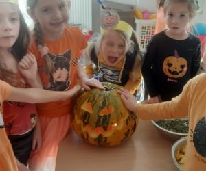 Dzieci stoją w półkolu obok stolika, na którym znajduje się wspólnie zrobiony lampion z wydrążonej dyni.
