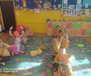 dzieci siedzą w dwóch rzędach, biorą udział w jednej z dyniowych konkurencji