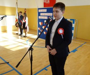 Uczeń w garniturze recytuje przy mikrofonie