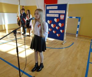 Uczennica w stroju galowym recytuje przy mikrofonie