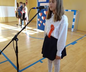 Uczennica w stroju galowym recytuje przy mikrofonie