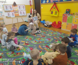 Dzieci wraz z nauczycielką siedzą na dywanie z misiami.