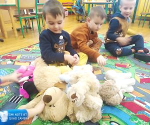 Dzieci siedzą z pluszowymi misiami.